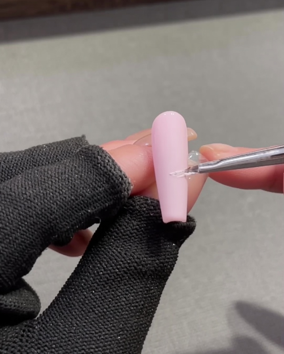 Un pennello a punta fine applica gel plastilina bianco per creare una linea del sorriso French su una base rosa.