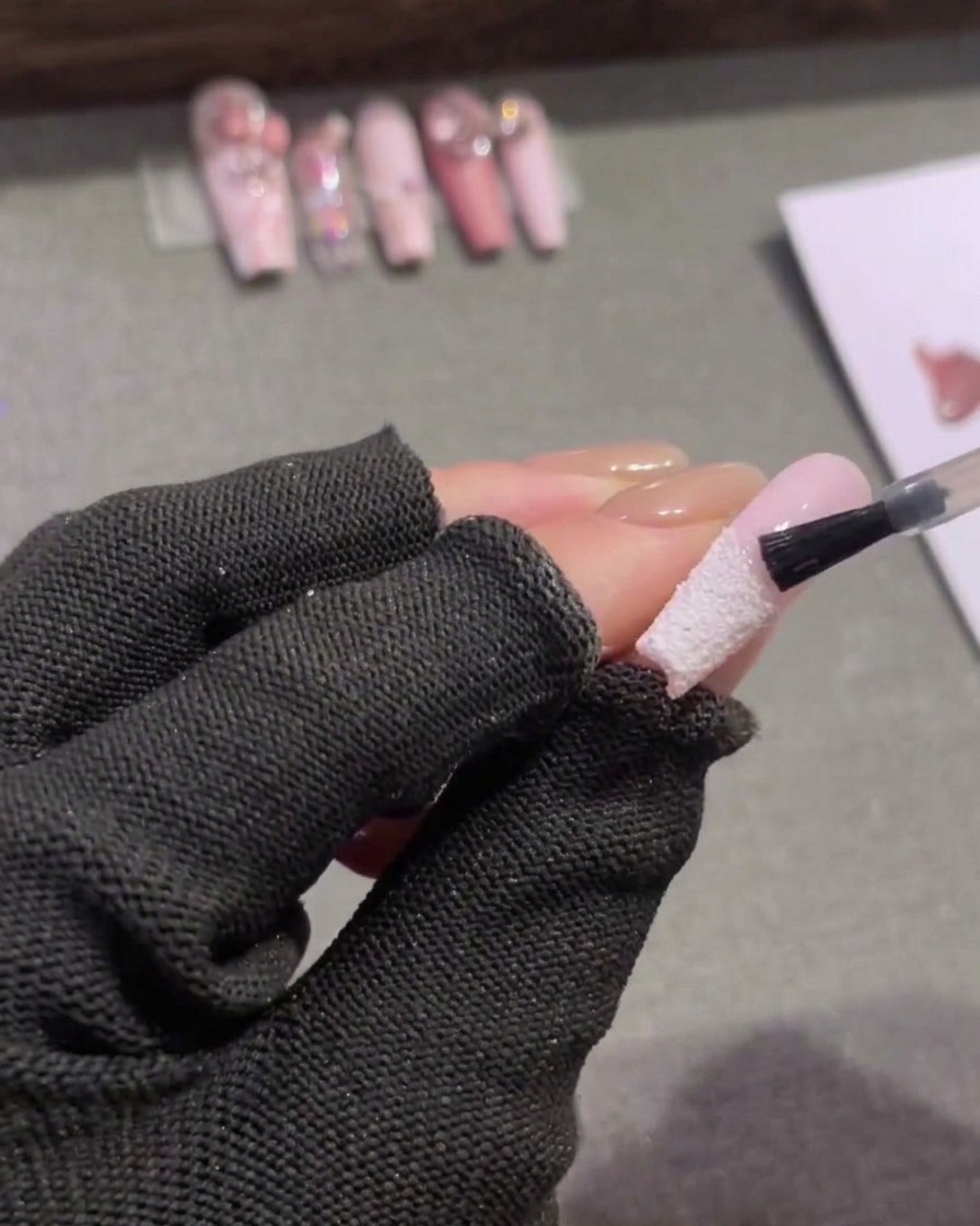 Un pennello applica un top coat opaco trasparente sulla metà superiore dellunghia, sopra la linea della French.