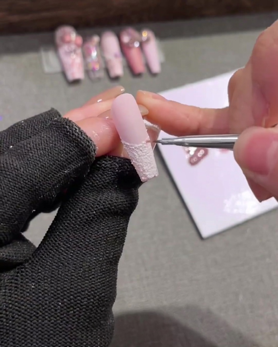 Dettaglio di un pennello liner che applica delicate strisce verticali rosa chiaro sopra la French bianca.