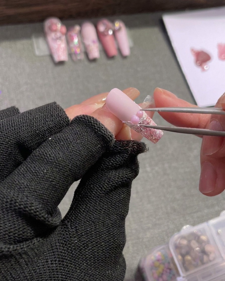 Pinzette posizionano strass argento e un charm a fiocco rosa vicino alla perla.