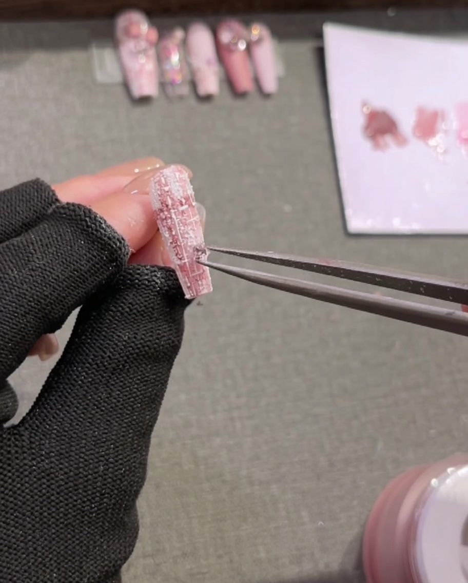 Pinzette posizionano piccoli strass su ununghia con design tartan.