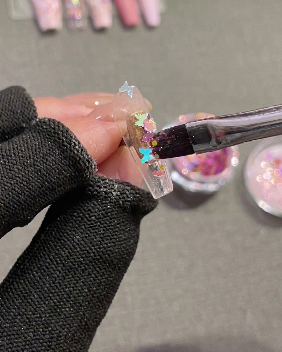 Un pennello posiziona paillettes a forma di farfalla su una tip con gel umido.