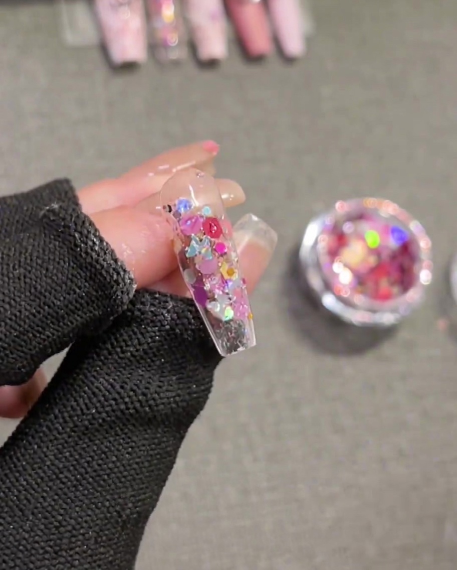Un pennello applica gel costruttore sopra ununghia decorata con paillettes.
