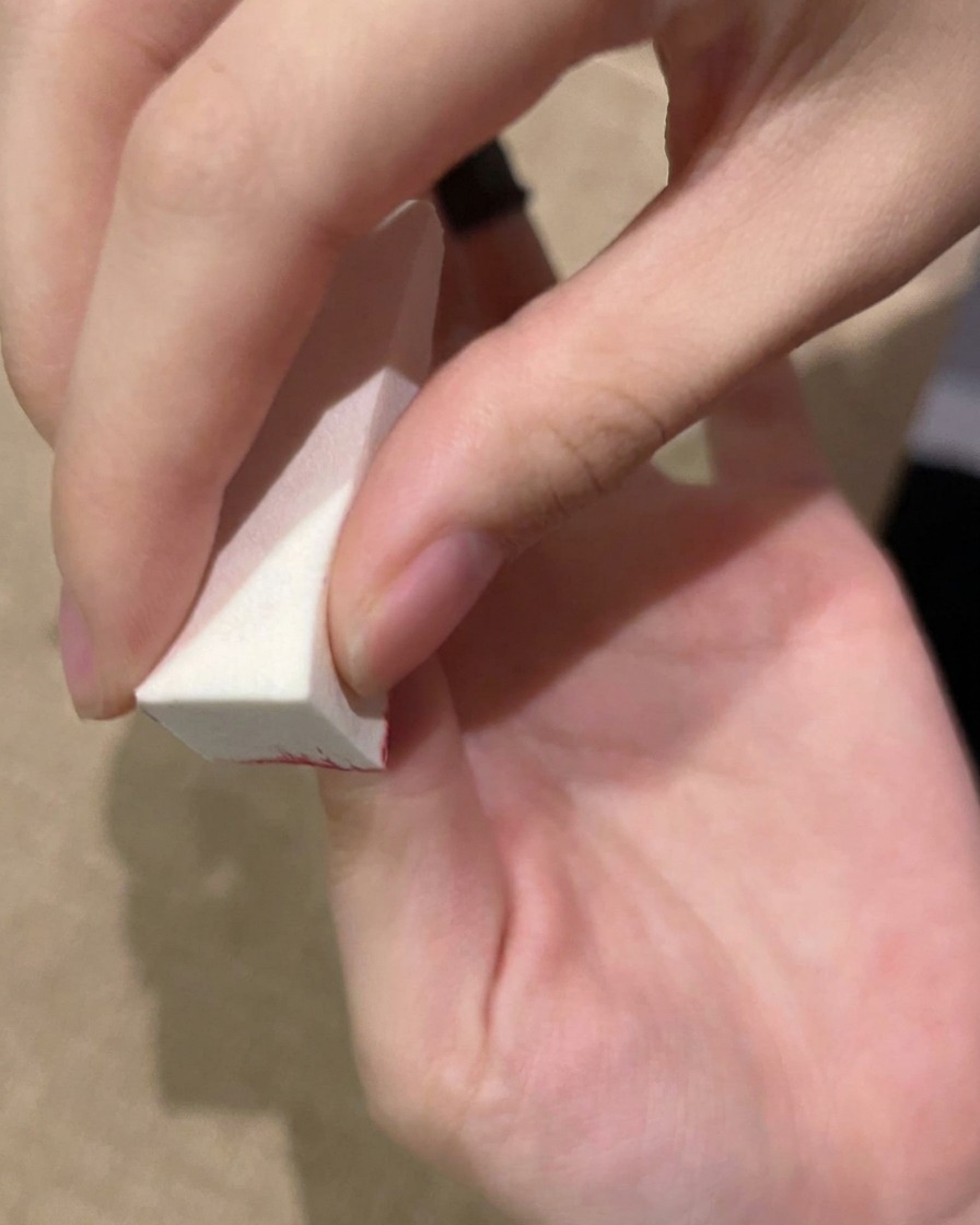 Una mano picchietta il gel su ununghia con una spugnetta prima della polimerizzazione sotto una lampada UV.