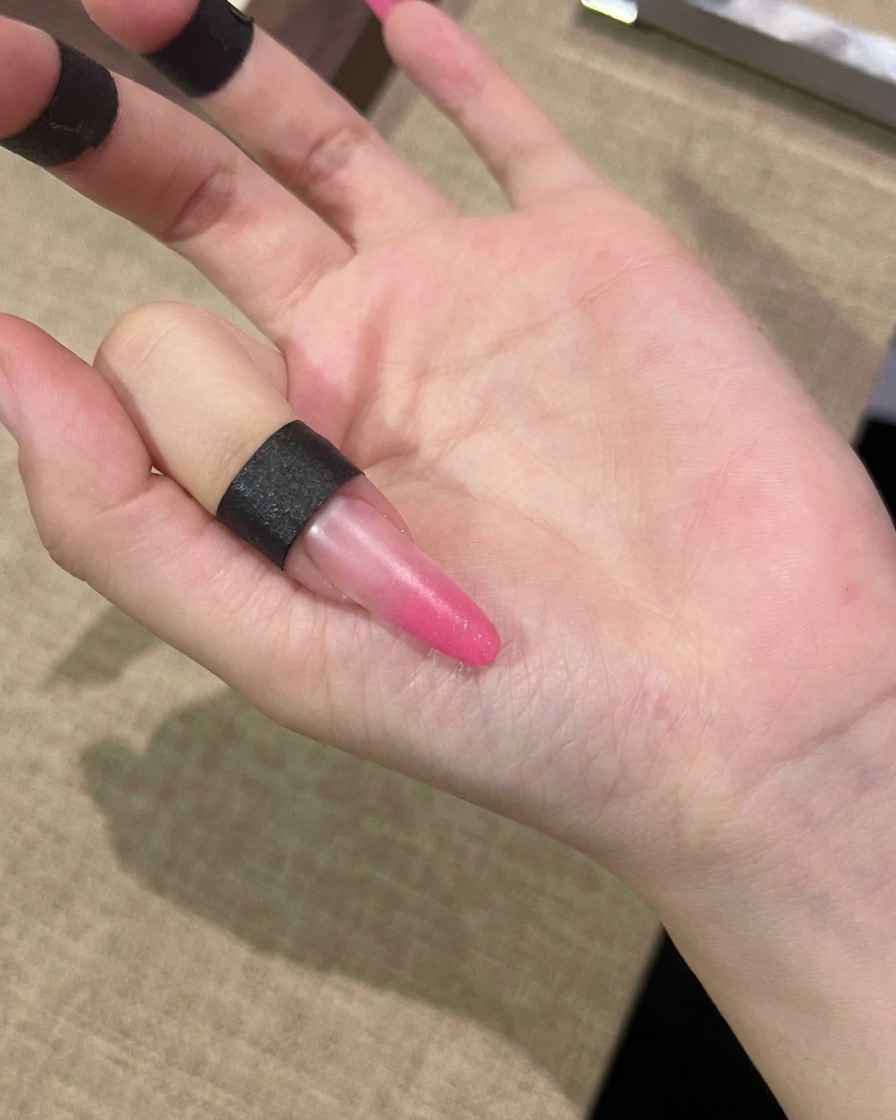 Un pennellino stende uno strato di gel cat-eye rosa sullintera superficie di ununghia.
