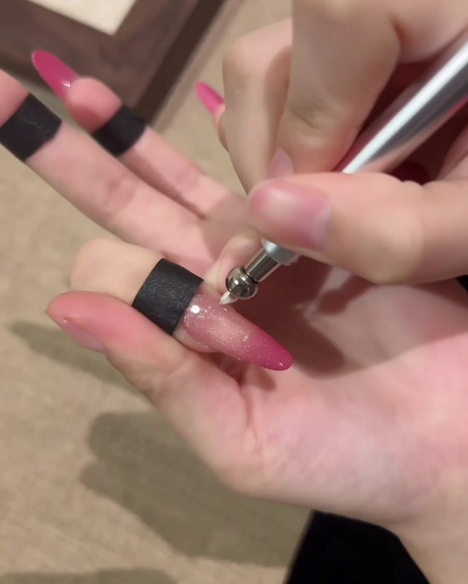 Primo piano di ununghia manipolata con uno strumento magnetico a penna per formare un effetto circolare a sfera cat-eye.