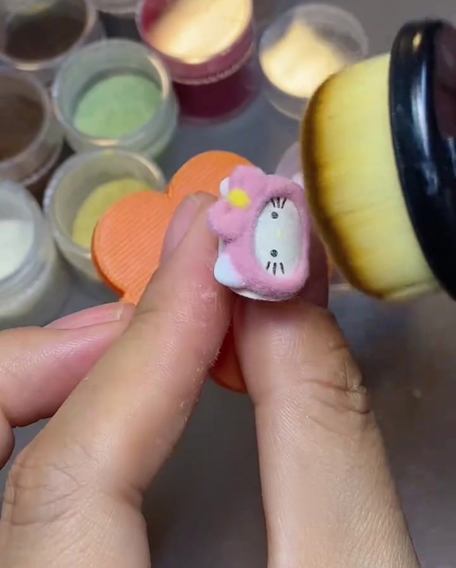 Primo piano di un pennello da trucco soffice che spazza via la polvere di velluto rosa in eccesso dalla superficie del charm.
