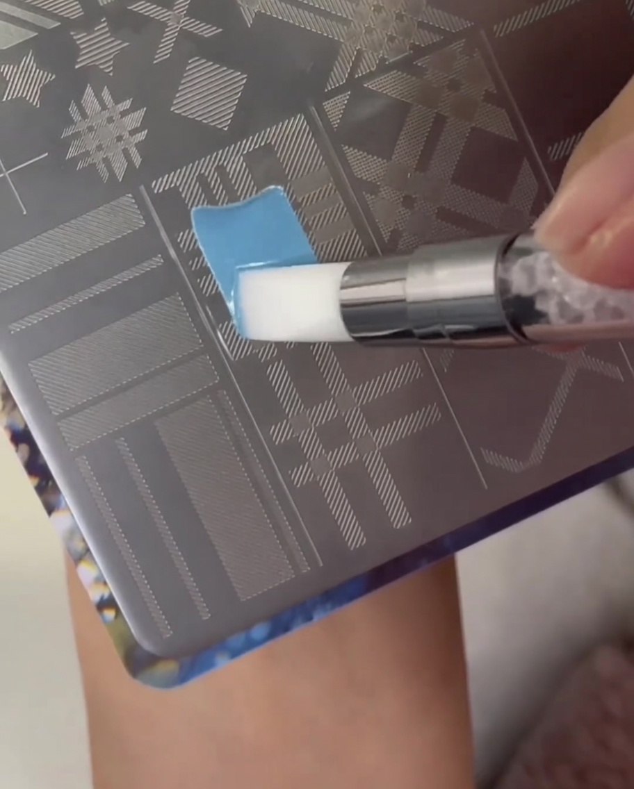 Un pennello applica smalto azzurro sopra una sezione con motivo plaid su un disco metallico per stamping.