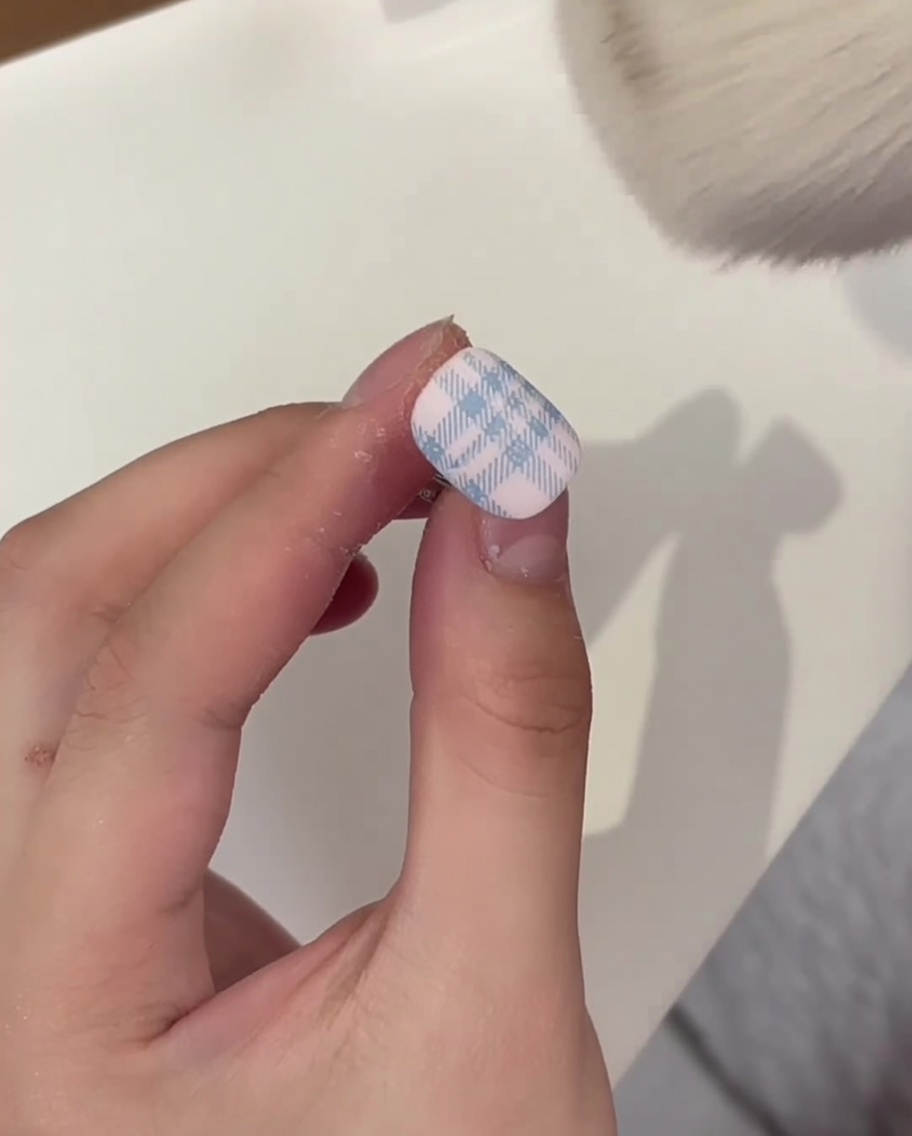 Un pennello da trucco soffice che rimuove leccesso di polvere cristallina bianca da ununghia con motivo plaid polimerizzato.