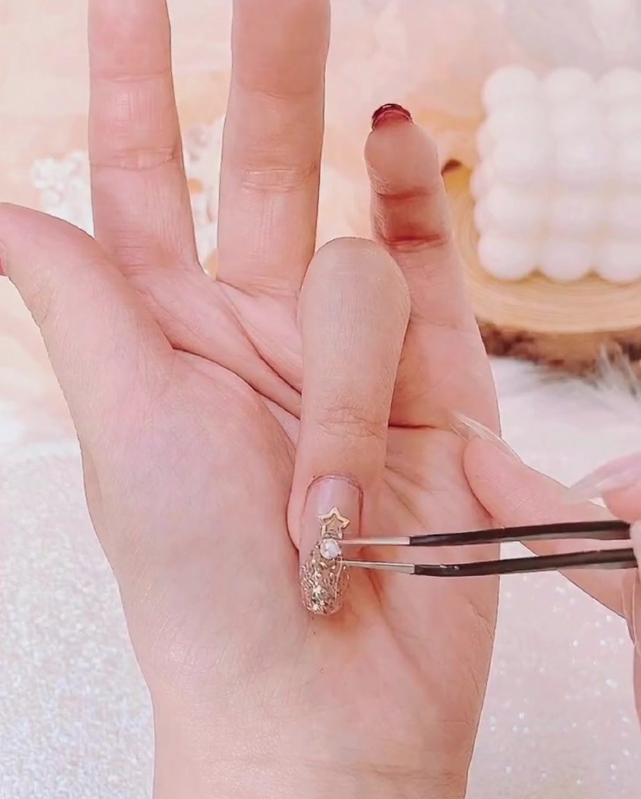 Pinzette che posizionano una piccola perla sotto la stella dorata tra altri piccoli strass.