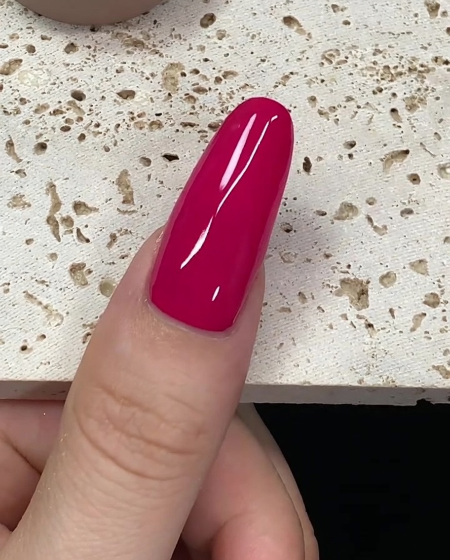 Un pennello carico di smalto gel rosso intenso che si avvicina alla cuticola di ununghia.