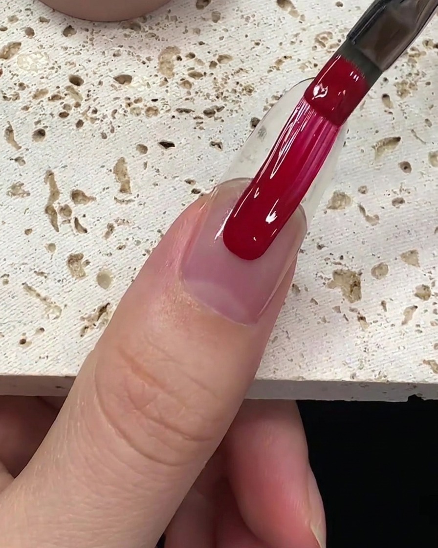 Unapplicazione uniforme di smalto gel rosso intenso steso lungo la lamina ungueale.