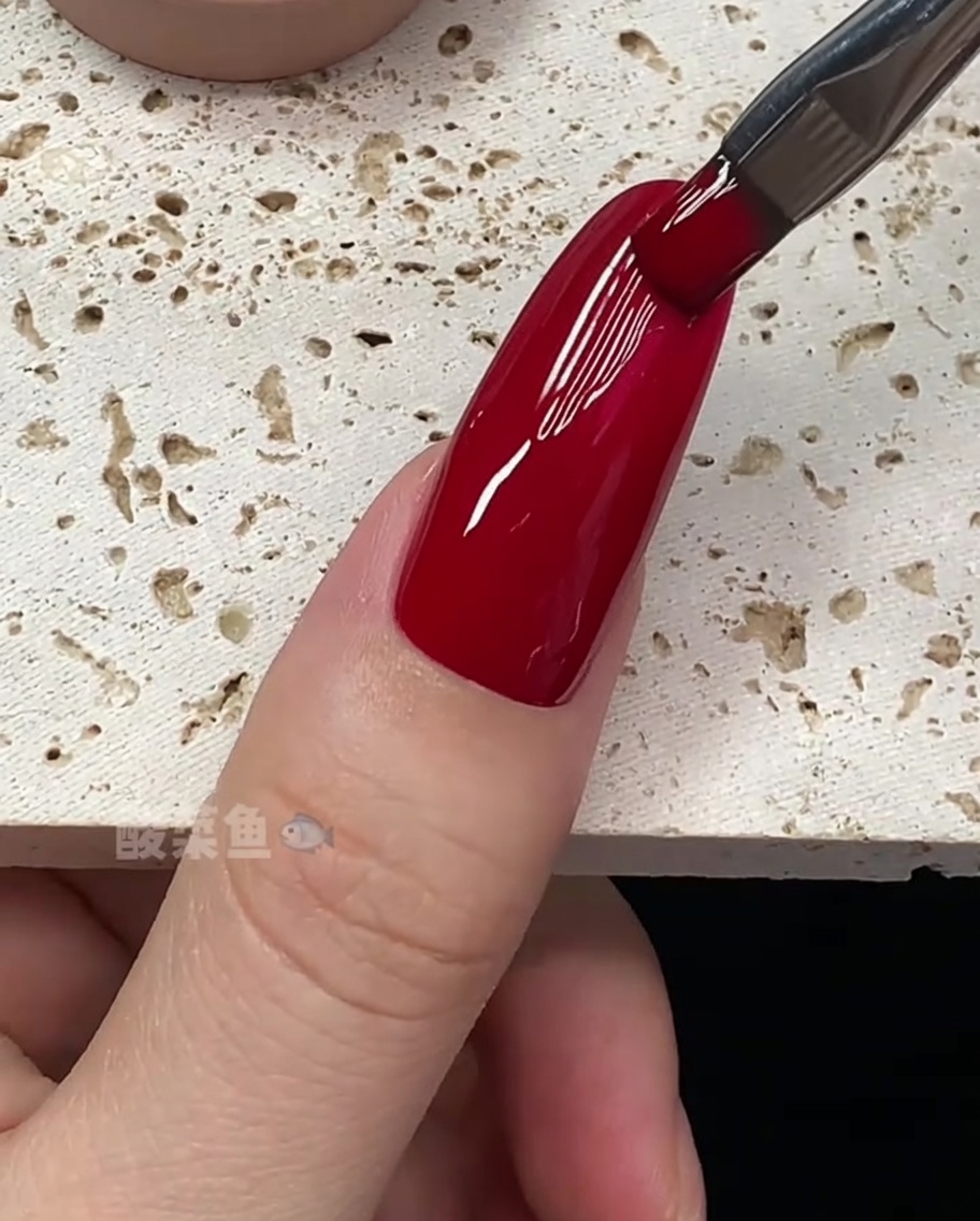 Primo piano di un pennello che perfeziona i bordi di ununghia rivestita di smalto gel rosso.