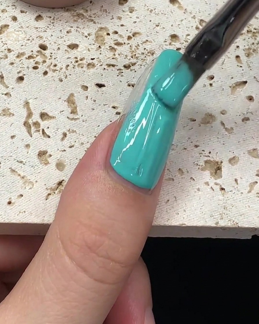 Una pennellata di smalto gel verde menta che viene tirata lungo il centro dellunghia.