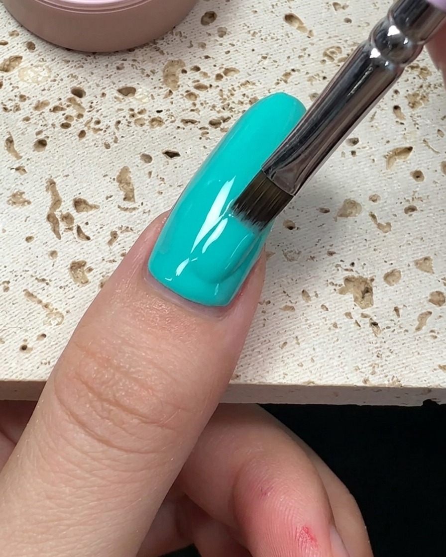 Primo piano che mostra le ultime pennellate di smalto verde menta che si livellano verso la fine dellunghia.