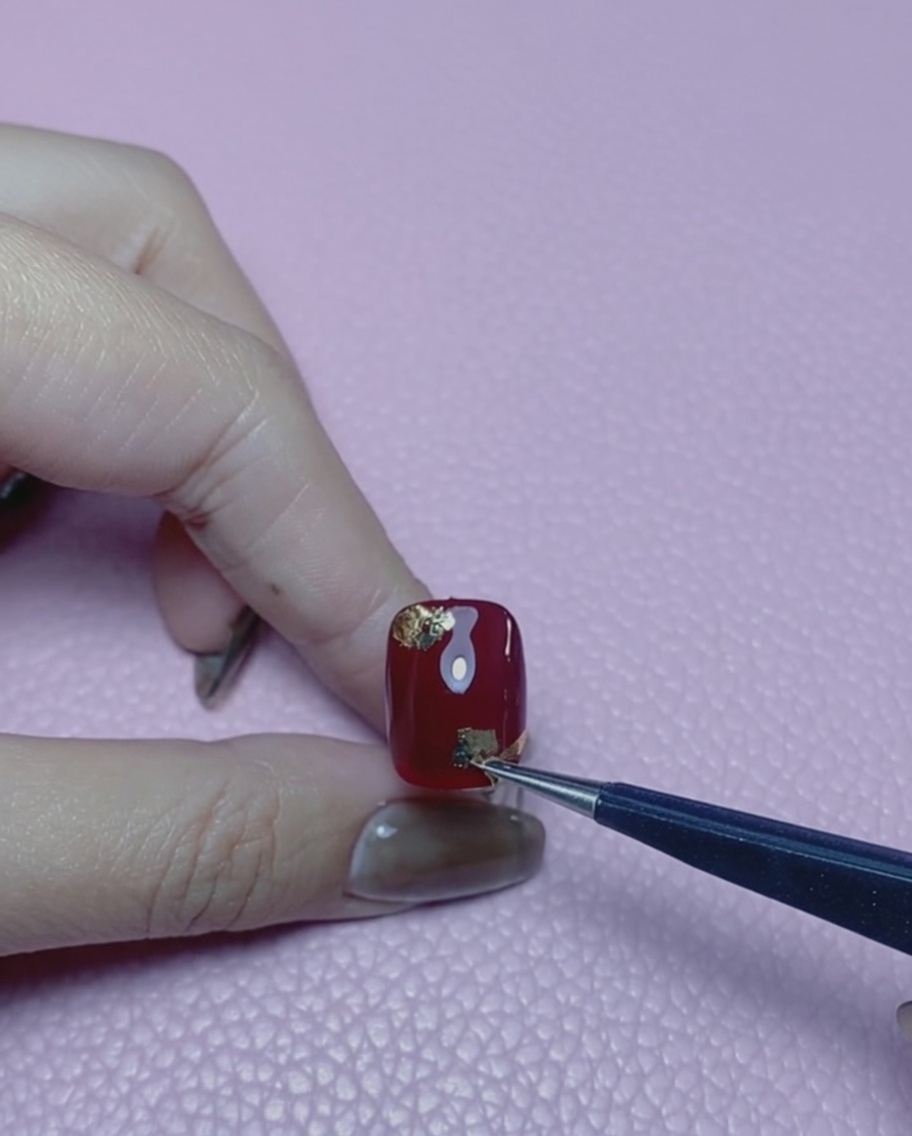 Uno strumento per unghie con punta in silicone che appiattisce le scaglie di foglia doro su ununghia rossa.