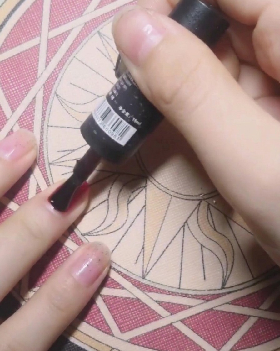 Il pennello di un flacone applica la base coat su ununghia in preparazione allo smalto gel colorato.
