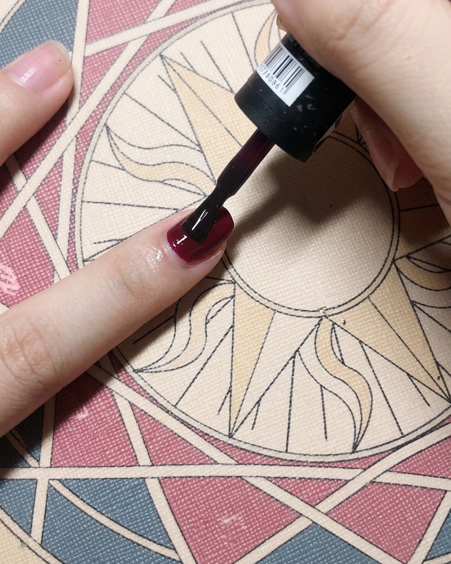Un pennello stende uno smalto gel bordeaux su una base coat per ottenere un colore pieno.