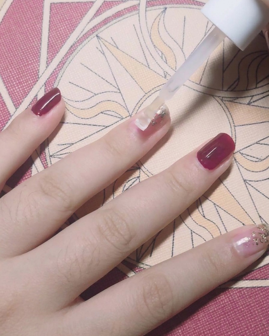Un pennello applica un top coat trasparente sopra ununghia decorata con foglia oro.