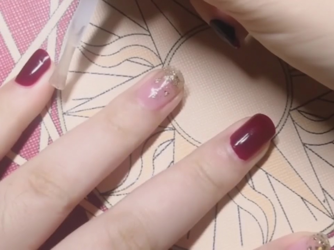 Applicazione di un top coat trasparente su ununghia smaltata di rosso.