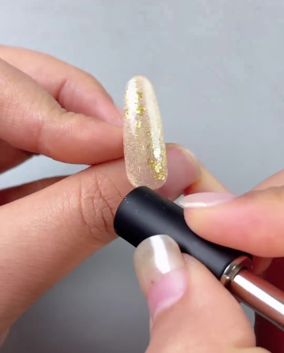 Un magnete per unghie tenuto vicino a ununghia dipinta con gel oro per creare una linea cat-eye riflettente.