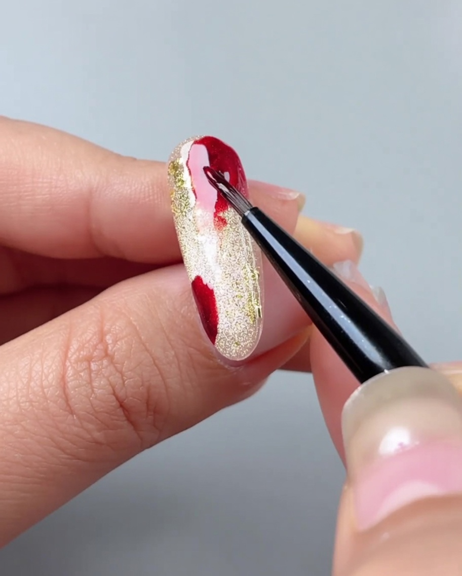 Un pennello per unghie sfuma le macchie di gel rosso creando un gradiente con gel acquerello.