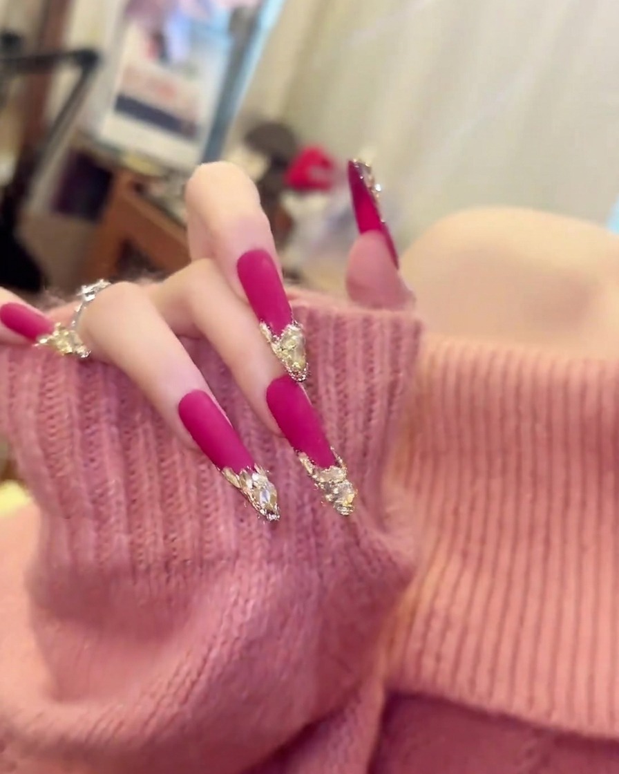 Una mano con un maglione rosa morbido che si muove leggermente per mostrare la lunghezza e la curvatura delle unghie lunghe a mandorla rosa opache.