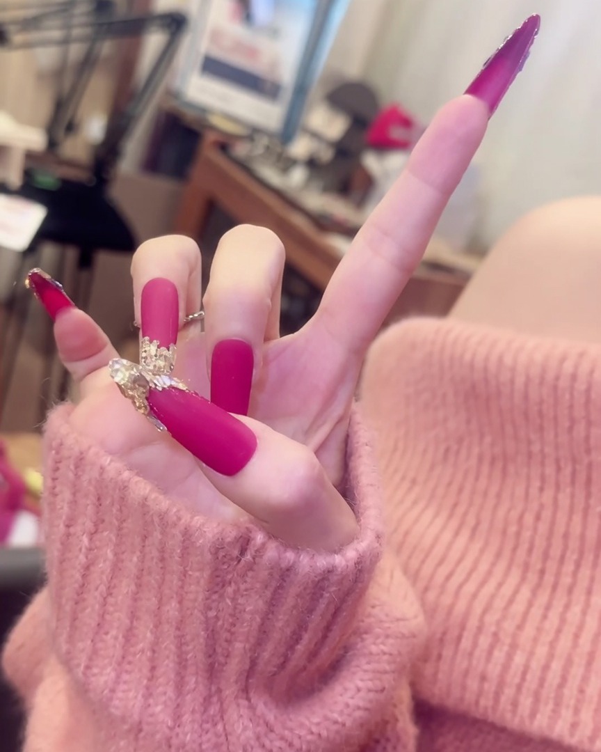 Una mano con le dita divaricate, che mostra lunghe unghie rosa opache con accenti di cristallo insieme a eleganti anelli dargento come accessori.