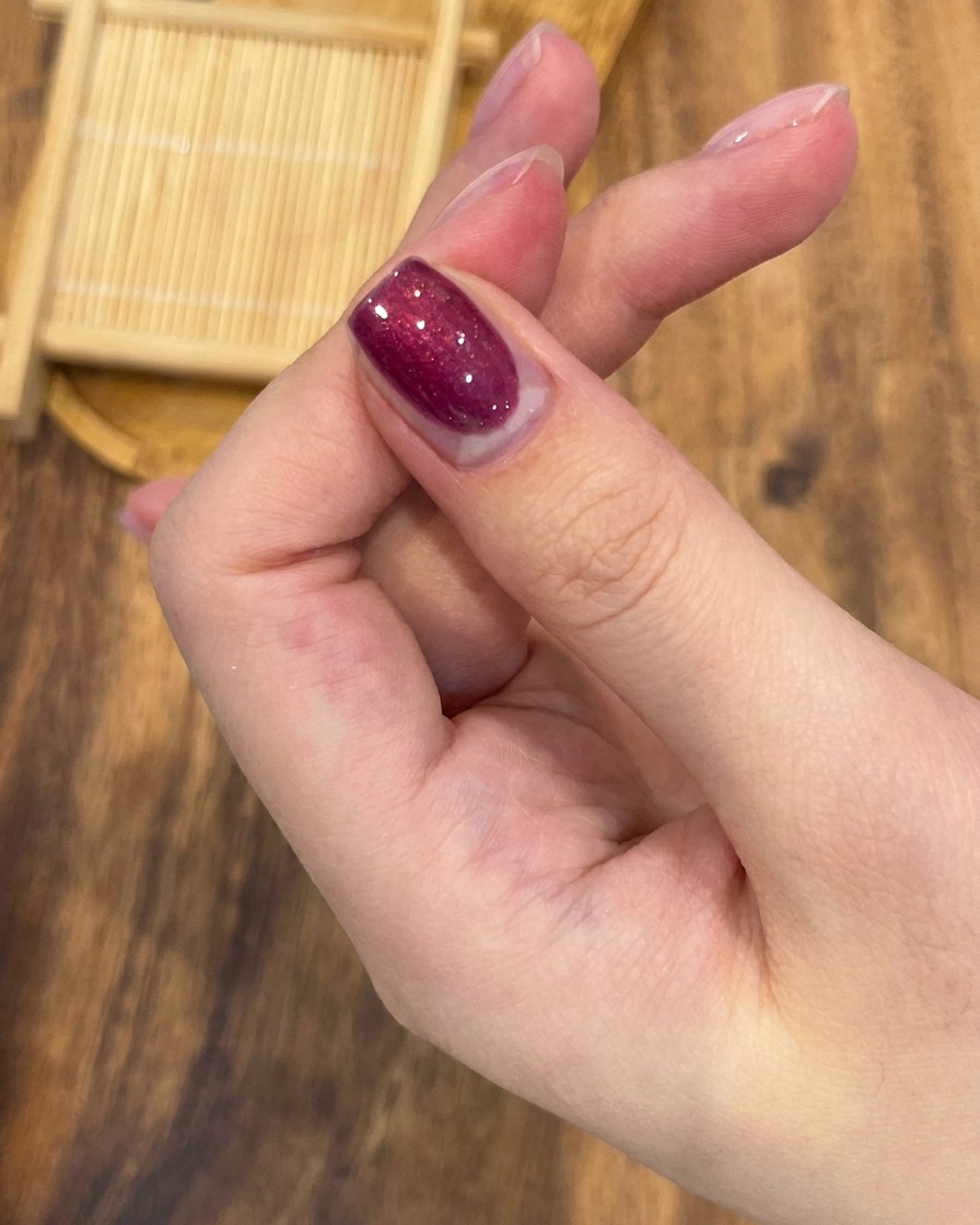 Un pennello professionale per unghie che stende uno strato uniforme di smalto gel magnetico color rosso rosa sullunghia.