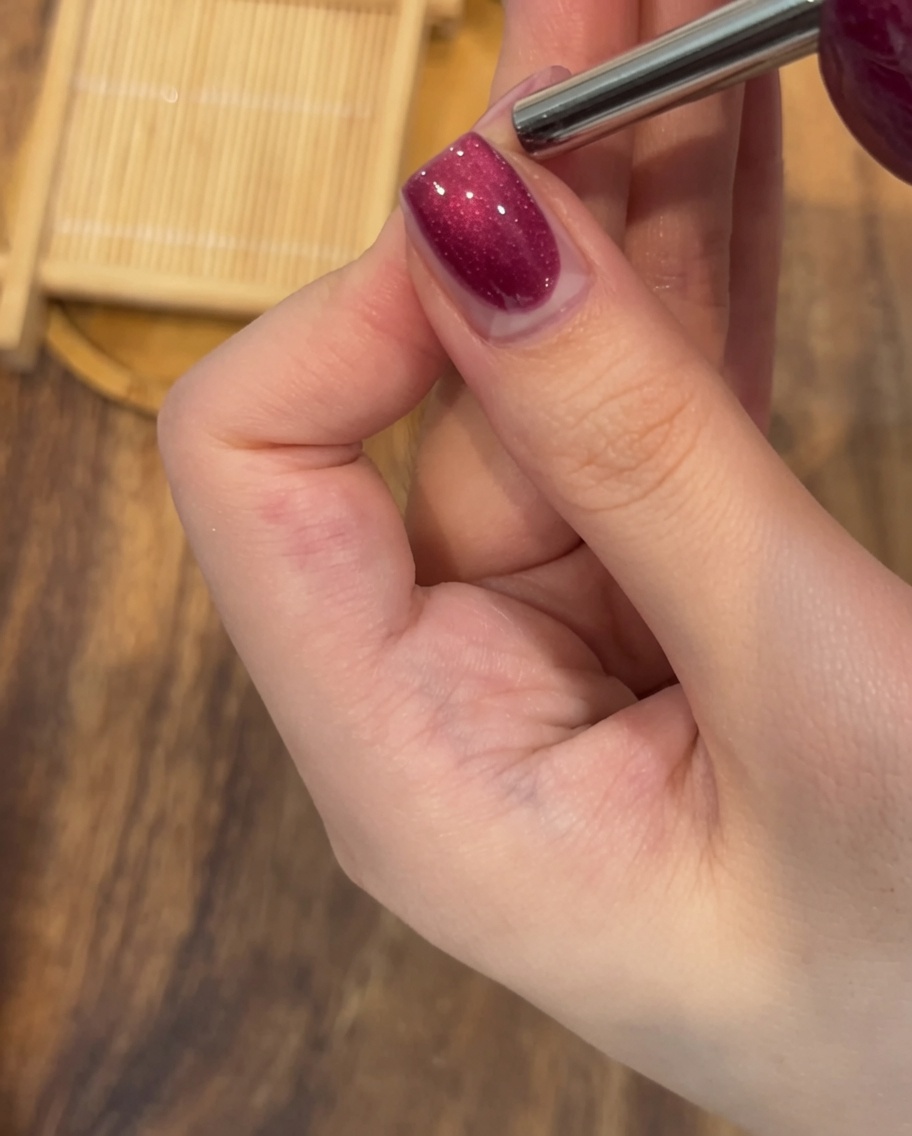 Primo piano di un magnete rettangolare tenuto fermo sopra ununghia smaltata con gel magnetico bagnato per creare una linea brillante e definita.