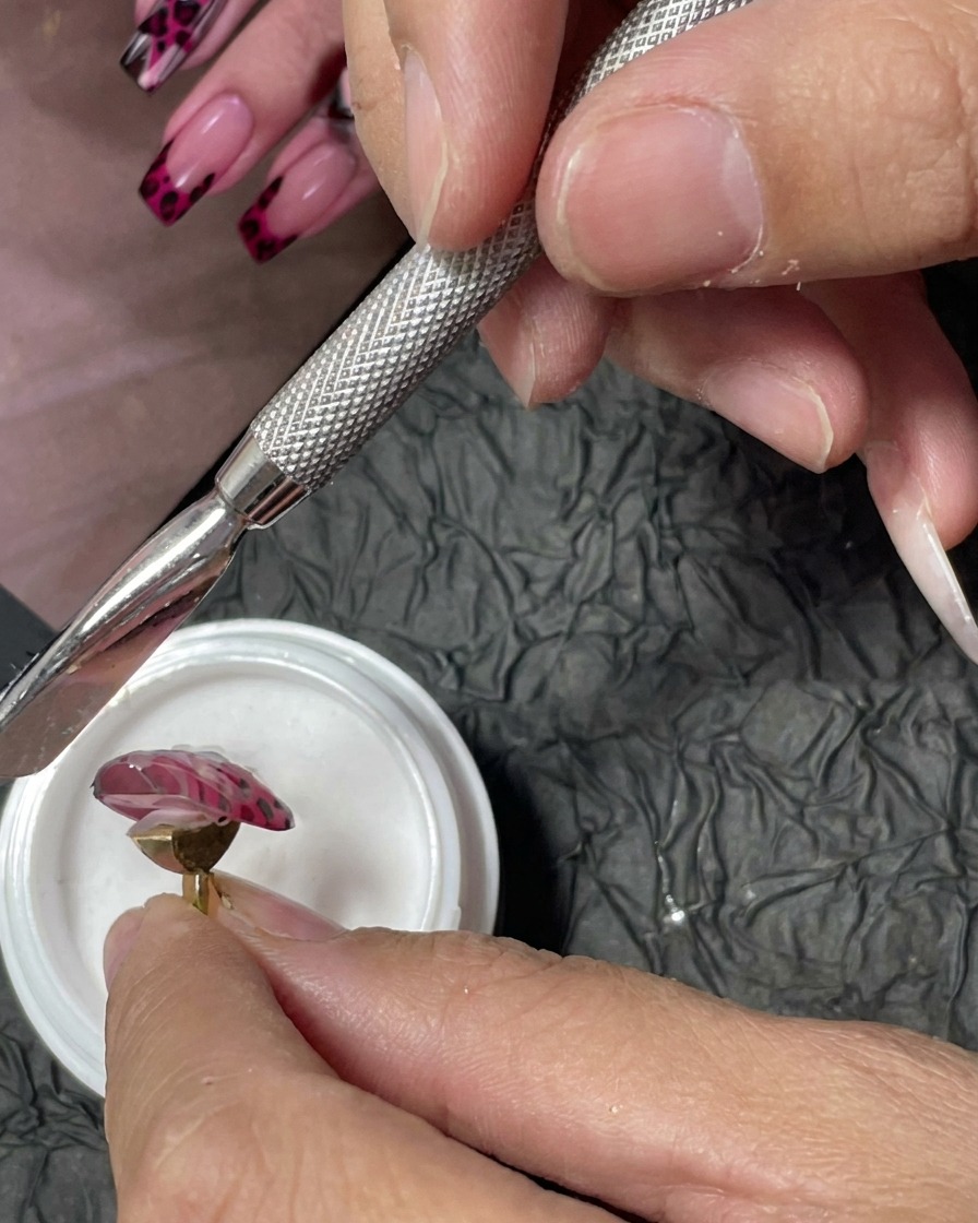 Uno strumento per manicure utilizzato per cospargere fine polvere acrilica bianca sui punti di gel rosso bagnati su ununghia rosa.