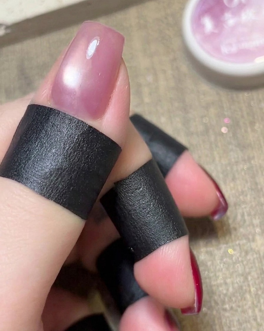 Un magnete cilindrico tenuto sopra uno smalto cat eye rosa ancora umido.