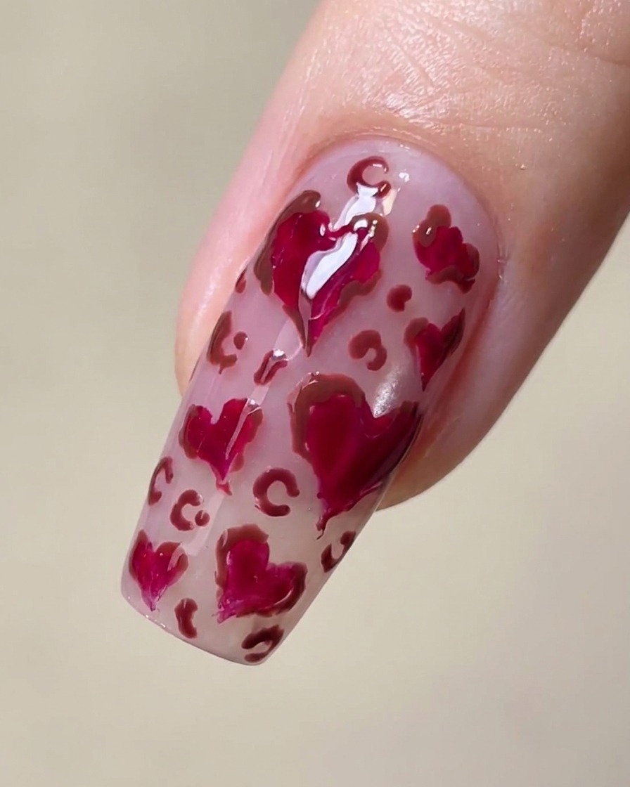 Primo piano di ununghia con cuori magenta e delicate macchie leopardate marroni negli spazi vuoti.