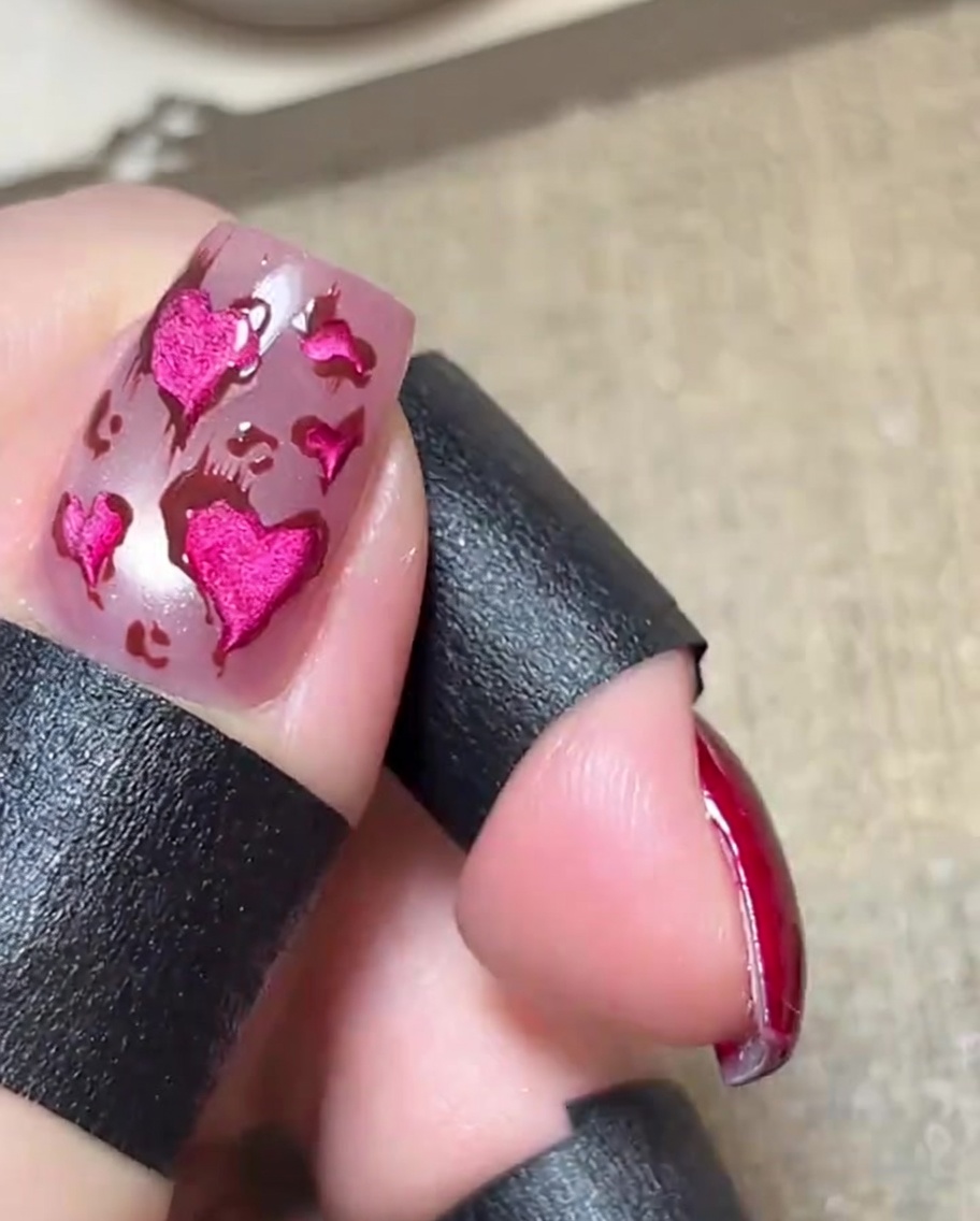 Primo piano di ununghia rosa lucida con cuori metallizzati delineati in marrone, con sottili linee marroni che si estendono dai disegni.