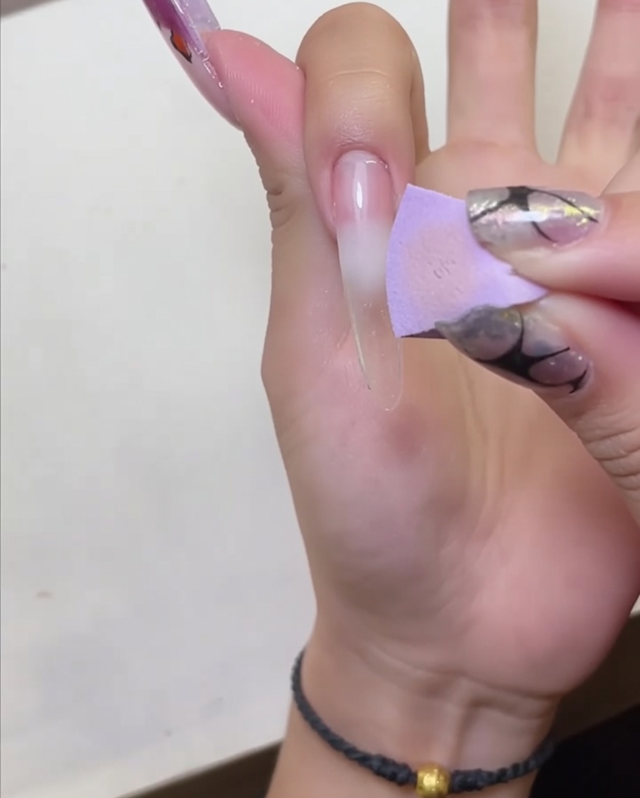 Una mano posizionata sotto una lampada LED per unghie per polimerizzare la base peel-off applicata.