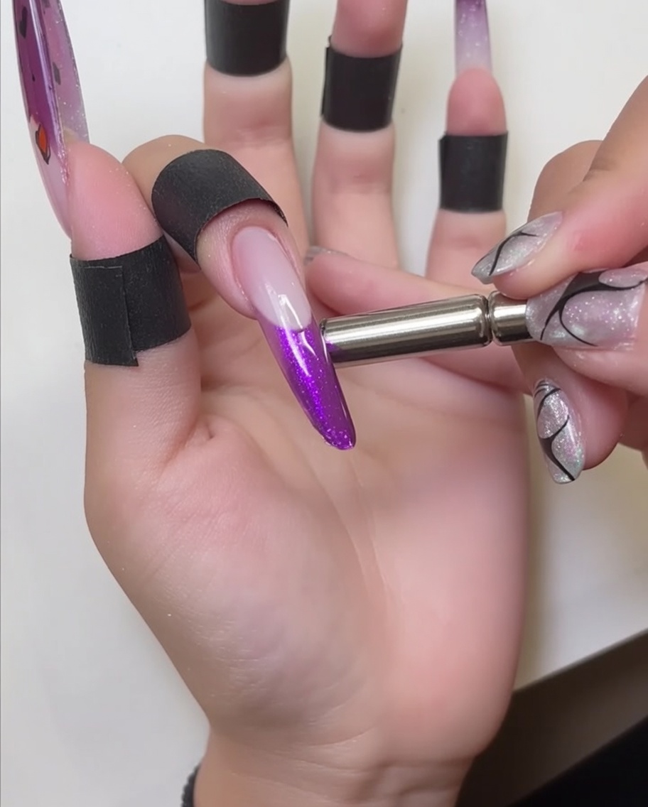 Un magnete tenuto vicino alla punta dellunghia, che mostra leffetto luccicante creato nello smalto cat-eye rosso.