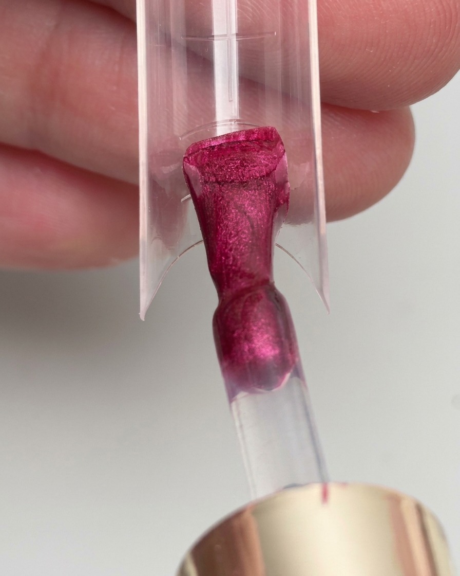 Un pennello che applica uno smalto gel magenta su una nail form trasparente.
