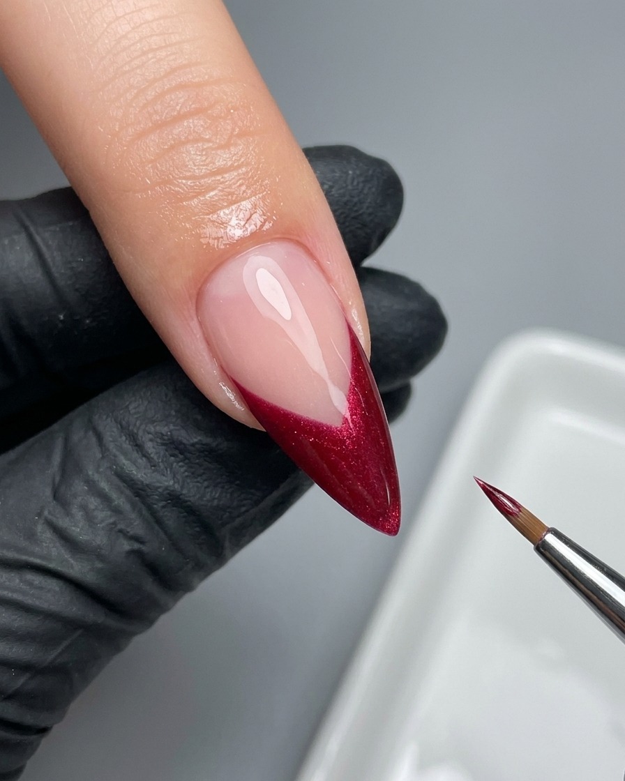 Un pennello liner sottile che perfeziona con cura il bordo di una French magenta su ununghia.