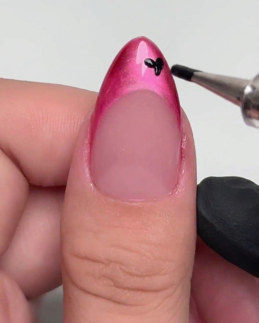 Un dotter che applica piccoli punti neri su una French dipinta di magenta.