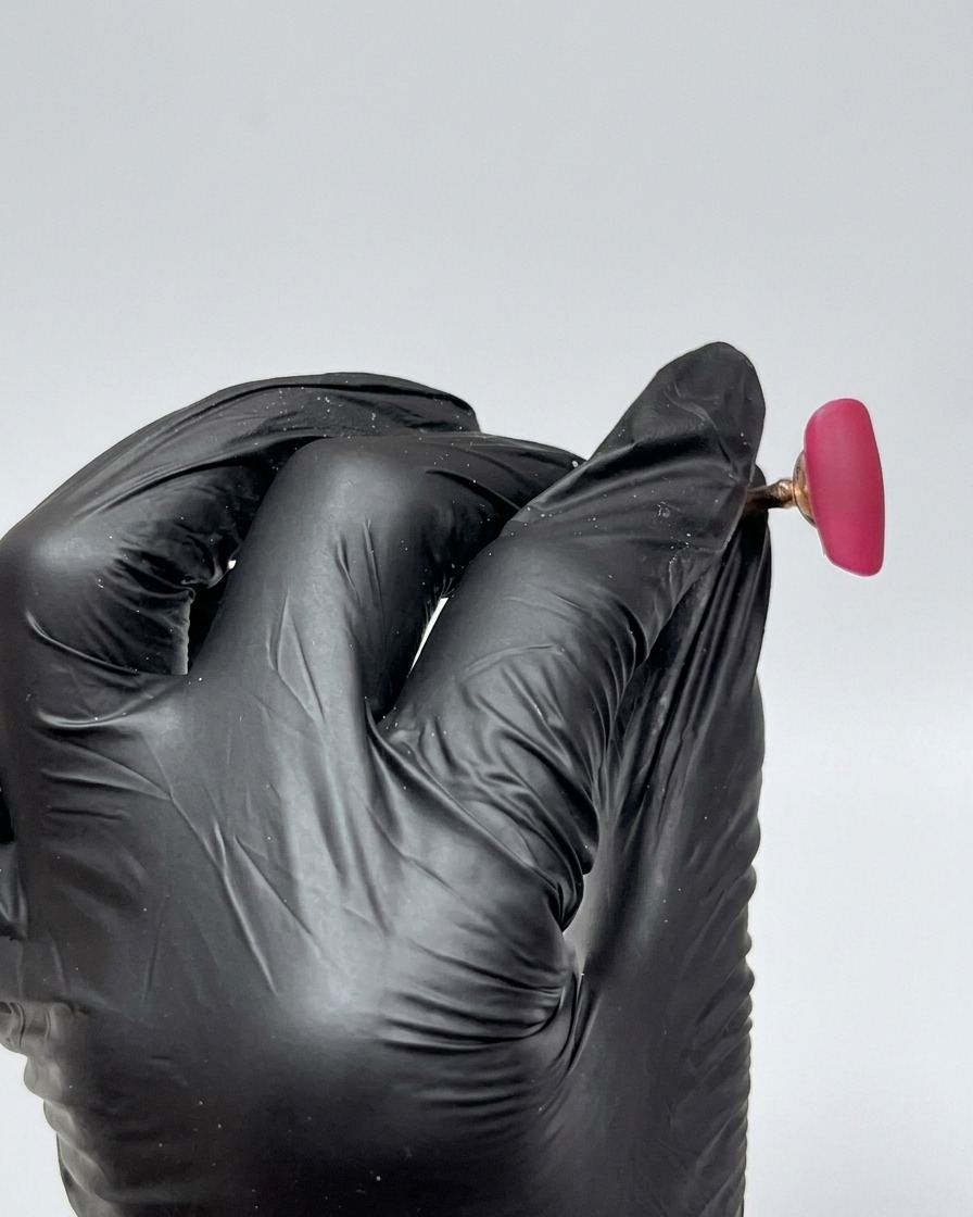 Primo piano di una tip interamente coperta da uno smalto gel rosa-rosso vibrante, con finitura liscia, lucida e non polimerizzata.