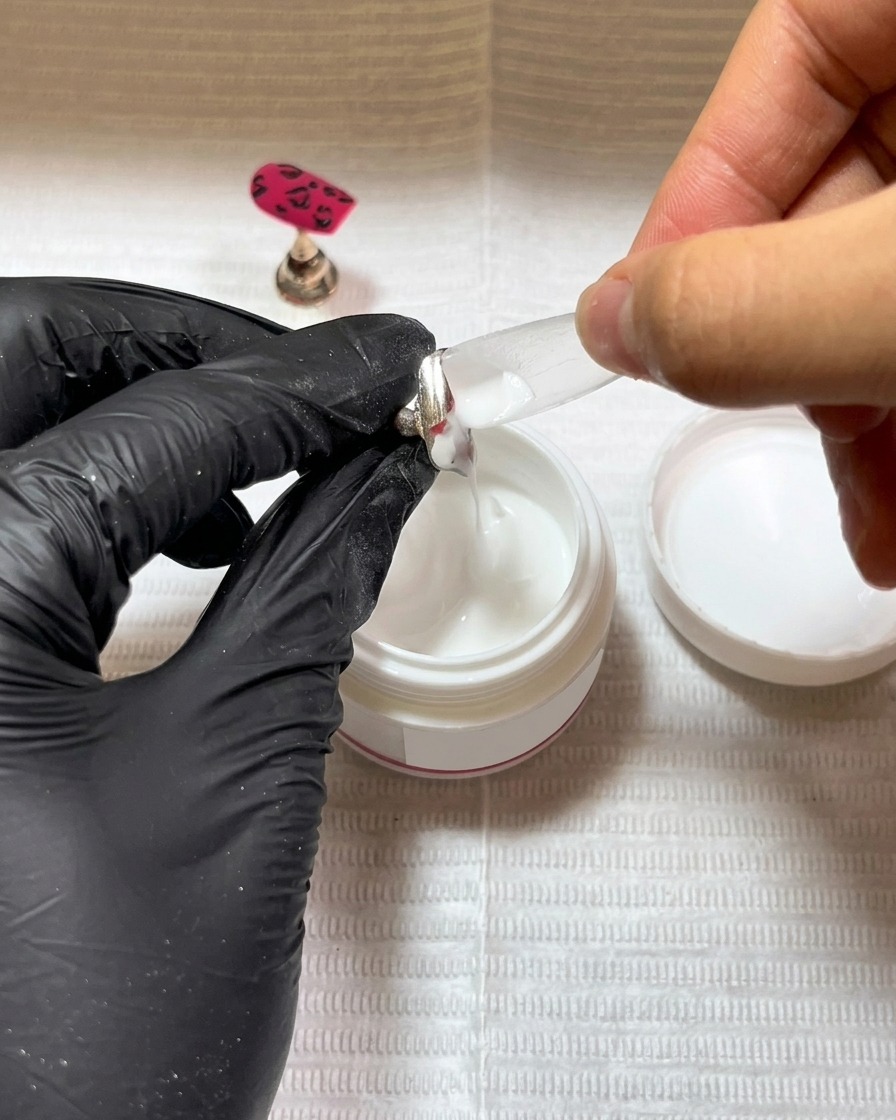 Un pennello applica un sottile strato di base coat in gel nero su una nuova tip.
