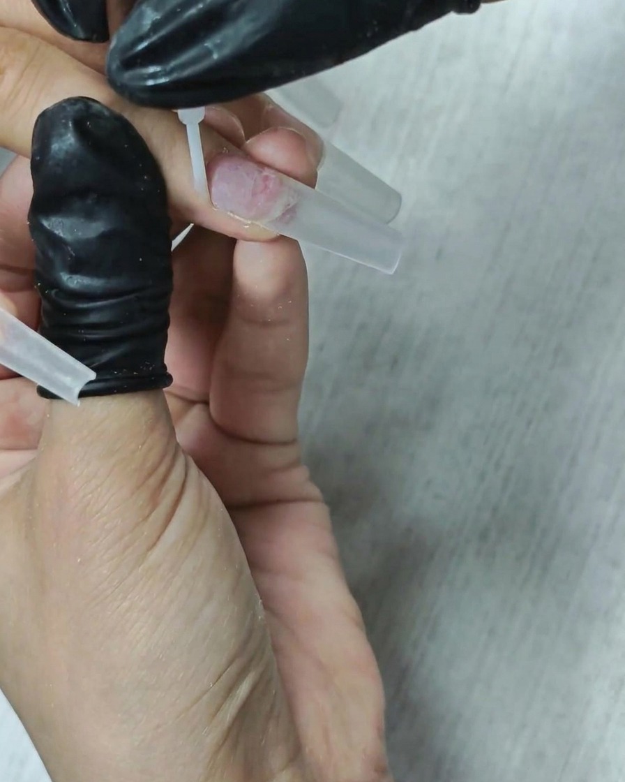 Un pennello applica un liquido deidratante trasparente sulla lamina ungueale.