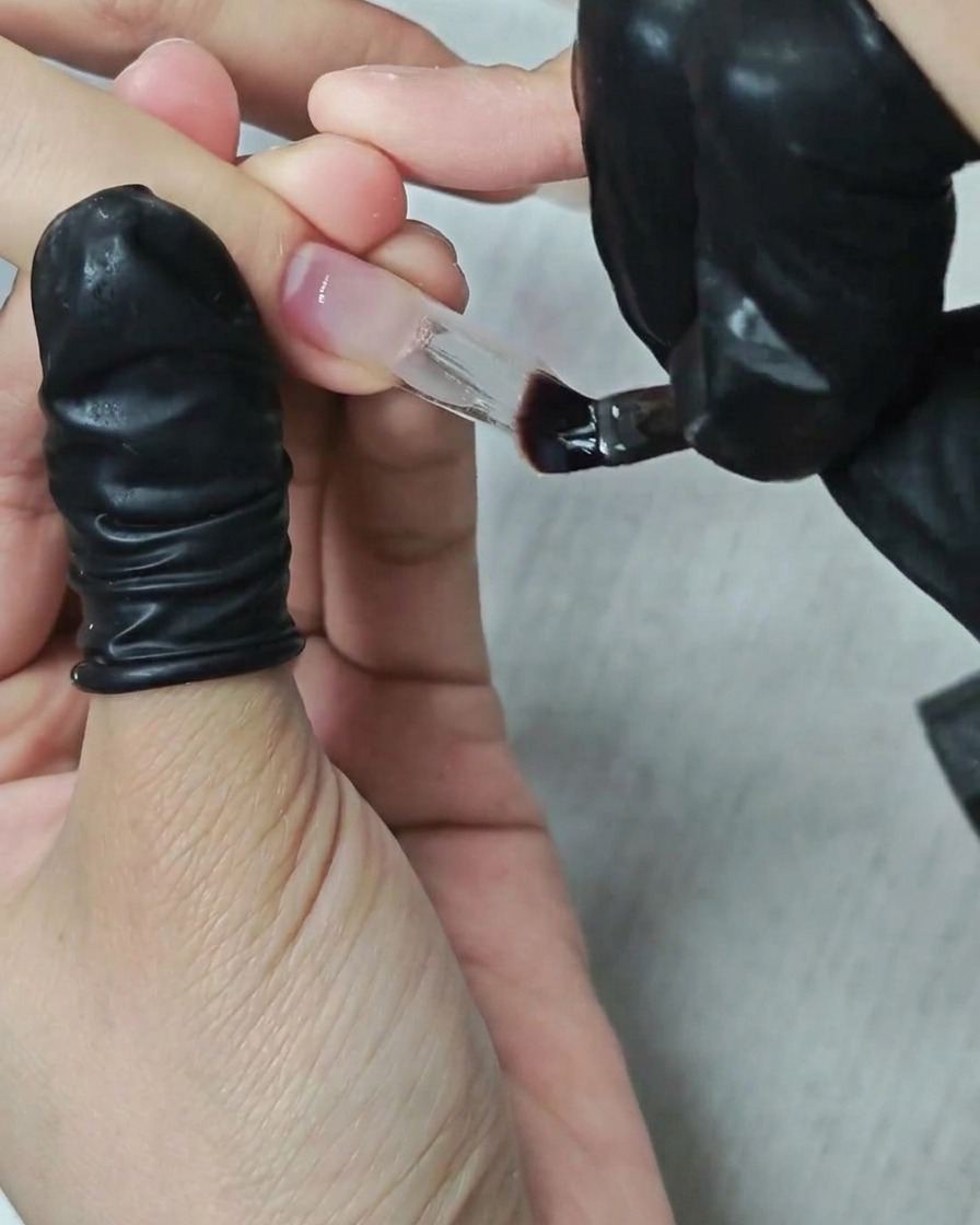 Unonicotecnica usa un pennello piatto per applicare e modellare un denso gel costruttore trasparente su unestensione quadrata.