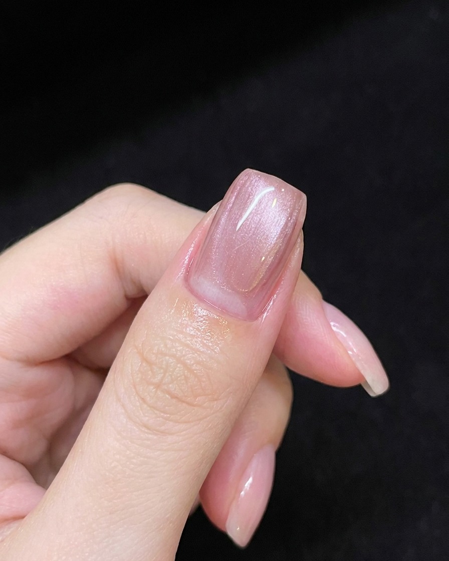 Una mano che tiene un magnete sopra ununghia rivestita di gel rosa per creare una linea di riflesso diagonale.