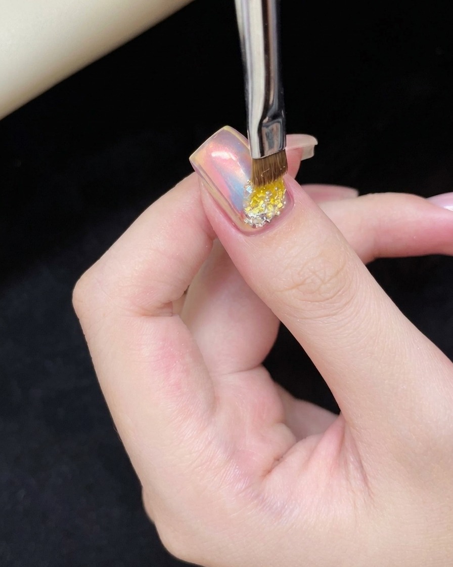 Un piccolo pennello per unghie che applica una goccia di gel adesivo trasparente sulla parte inferiore di ununghia cat-eye rosa.
