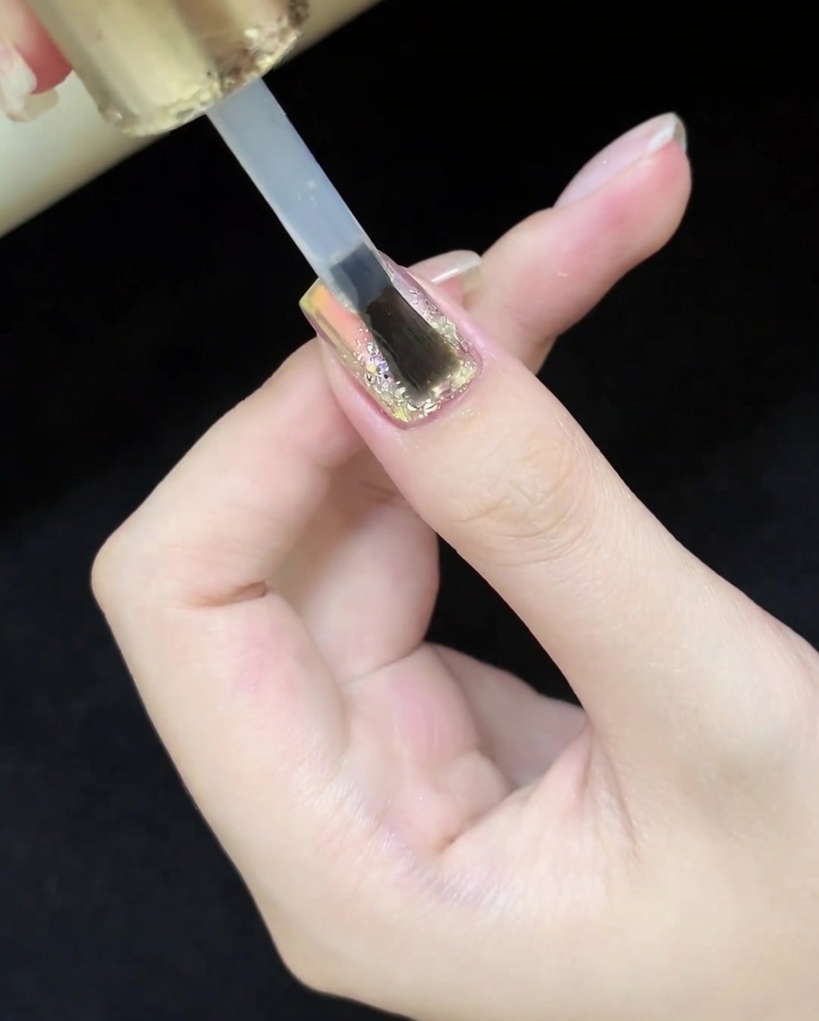 Un pennello che applica un top coat trasparente e lucido sopra il design completo con glitter e cat-eye.