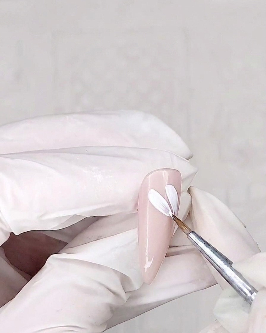 Un pennello di precisione dipinge petali bianchi su ununghia con base rosa.