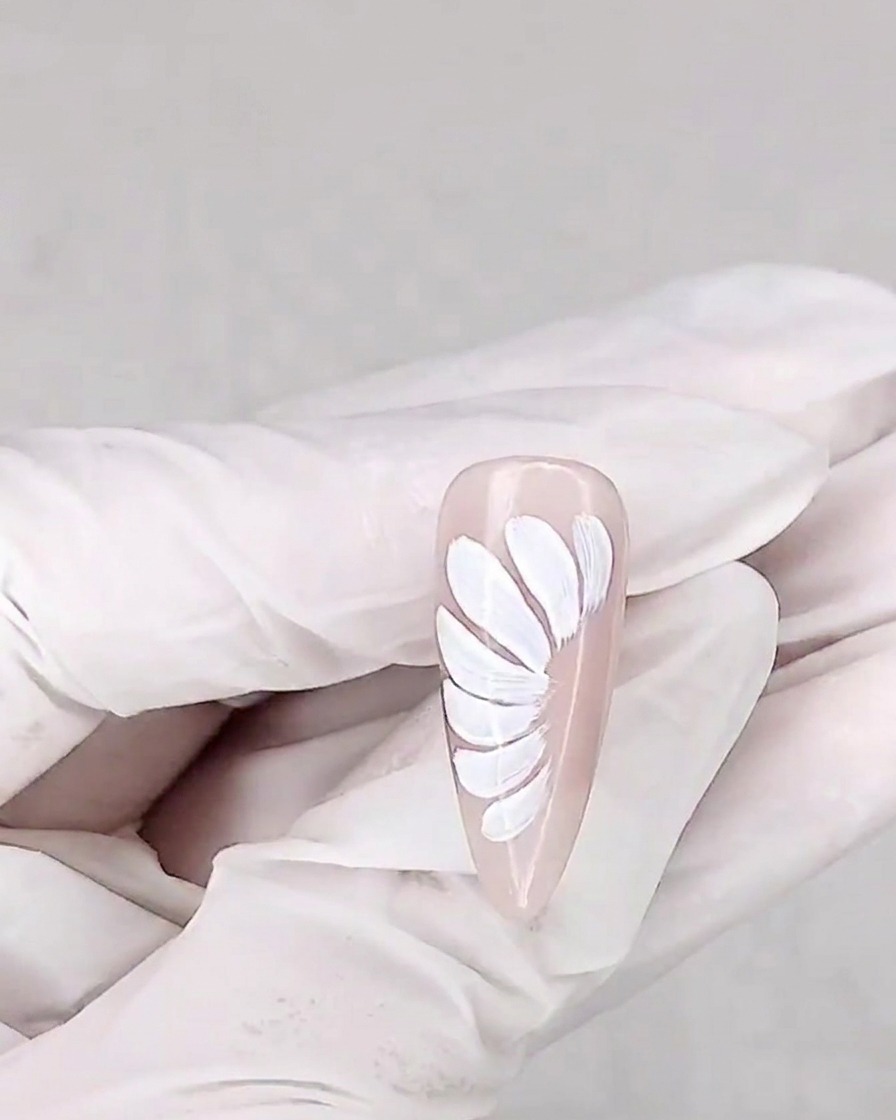 Un pennello applica un top coat opaco sopra lunghia decorata con margherite.