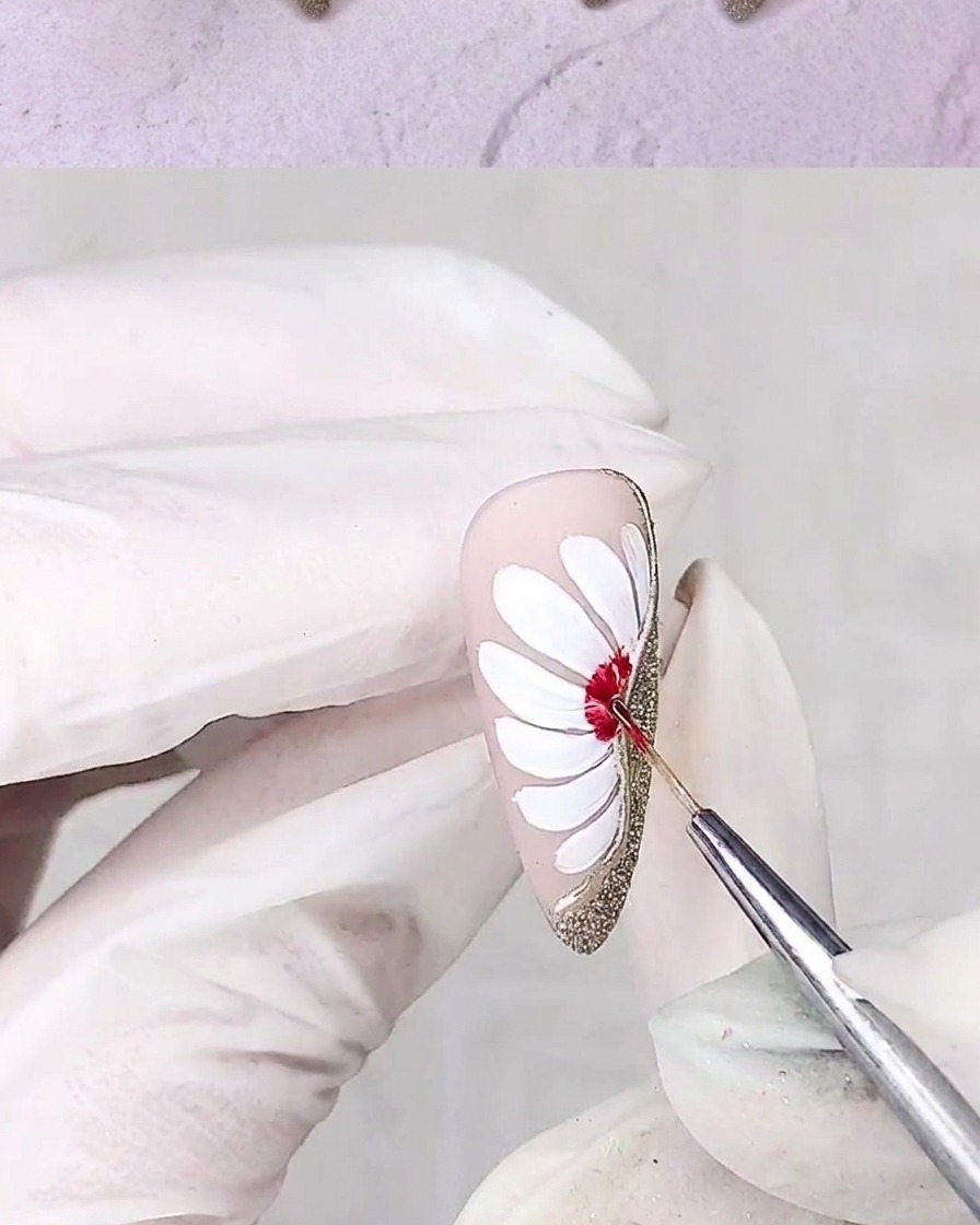Un pennello di precisione applica gel rosso al centro del design di una margherita bianca su ununghia.