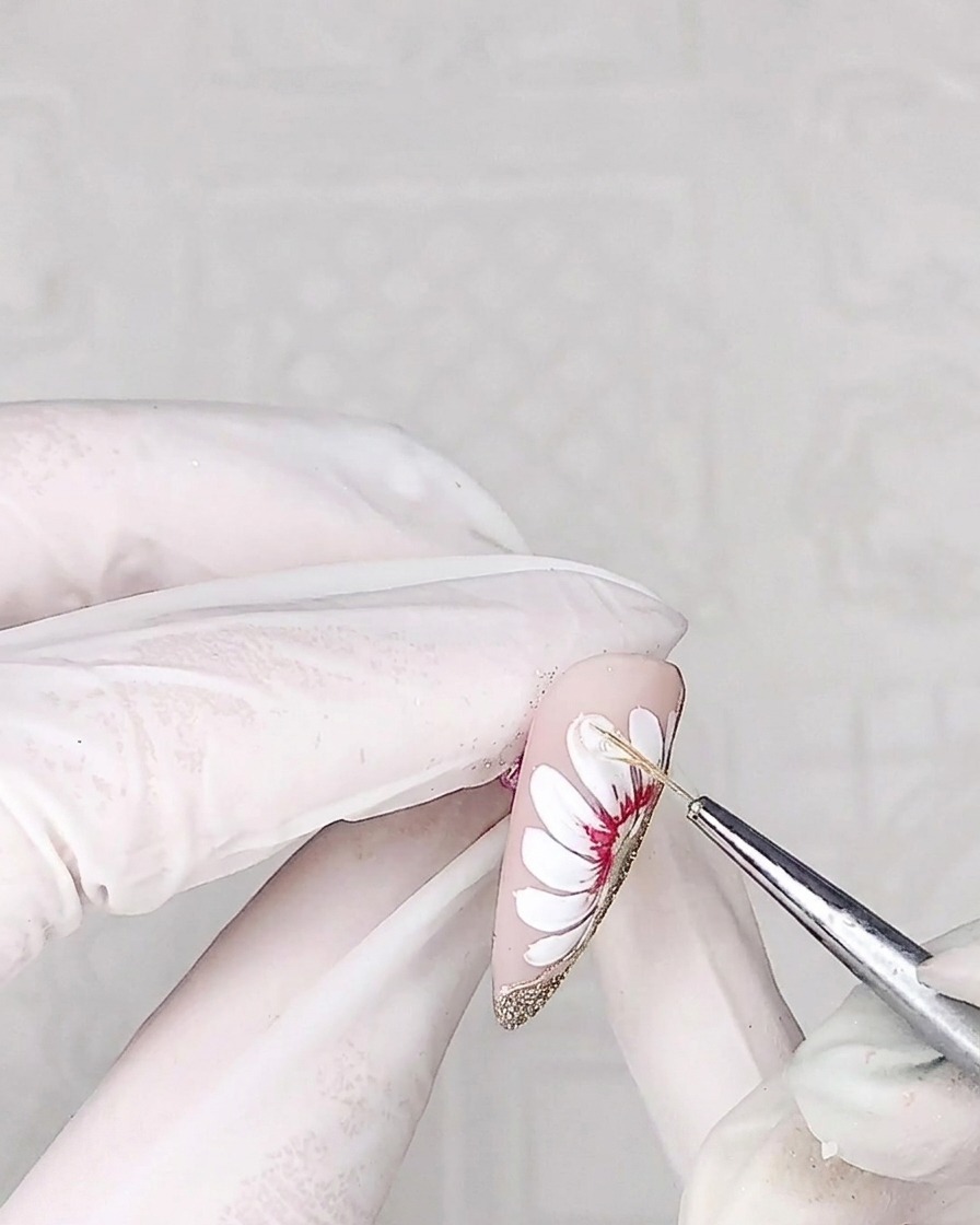 Primo piano di un pennello liner che applica un gel adesivo trasparente e denso sulla superficie di un petalo di margherita.